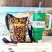 A purple & yellow swirl print bag, is pictured beside a Stanley 40 ounce Quencher, money & chap stick. Eyeglasses hang from a zipped pocket.